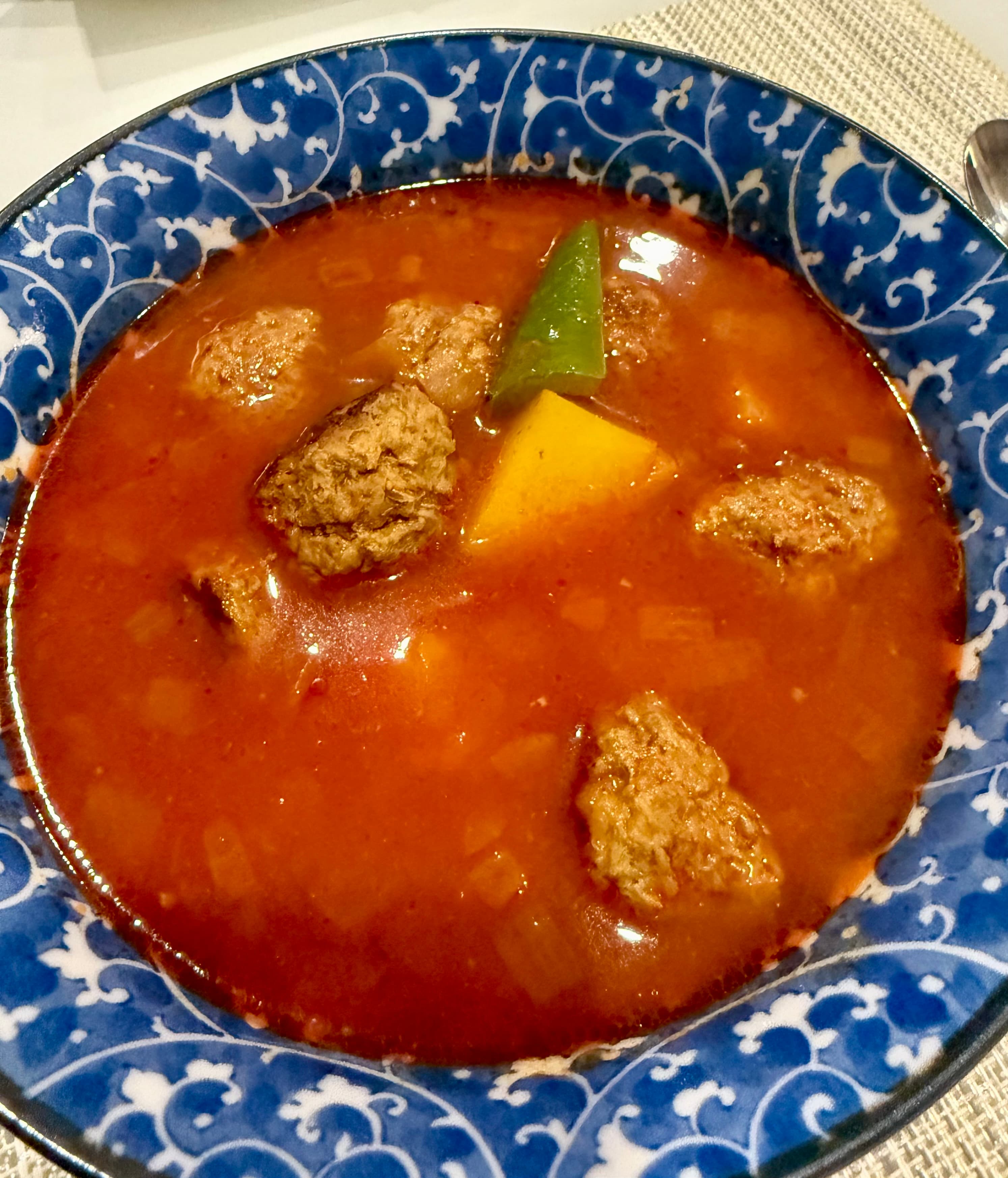 A bowl of beef and potato soup in a blue and white patterned bowl, with chunks of beef, potato, and jalapeño in a rich tomato broth