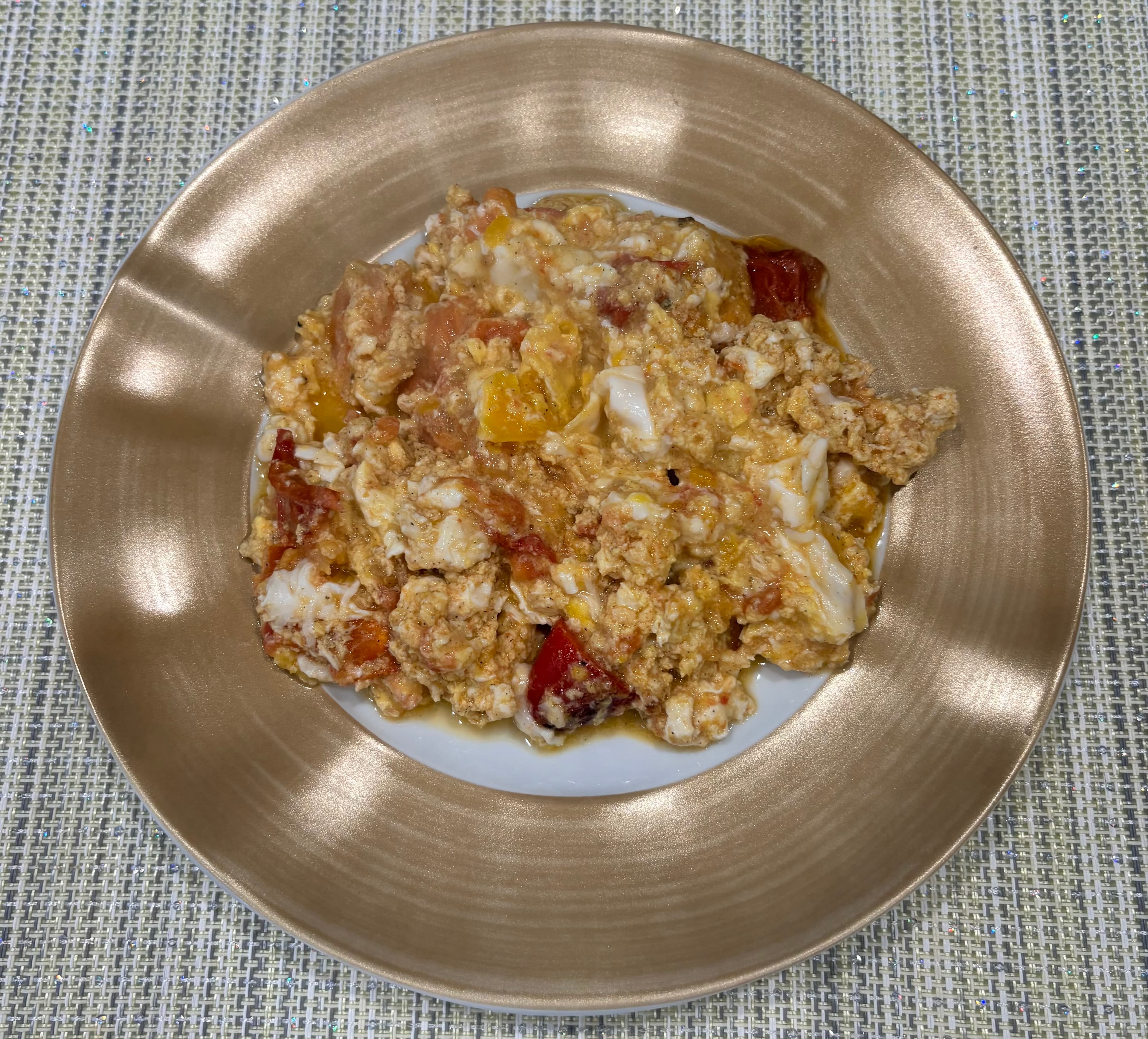 A gold-rimmed plate of tomato jalapeño omelet, with scrambled eggs, tomato, and jalapeño